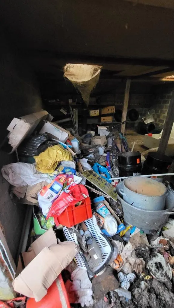 Cave encombrée de déchets, de cartons et d'objets entassés.