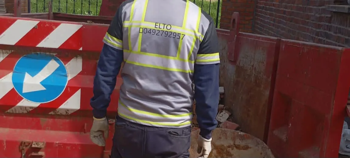 Ouvrier ELTOGROUP devant une benne de déblais sur un chantier.