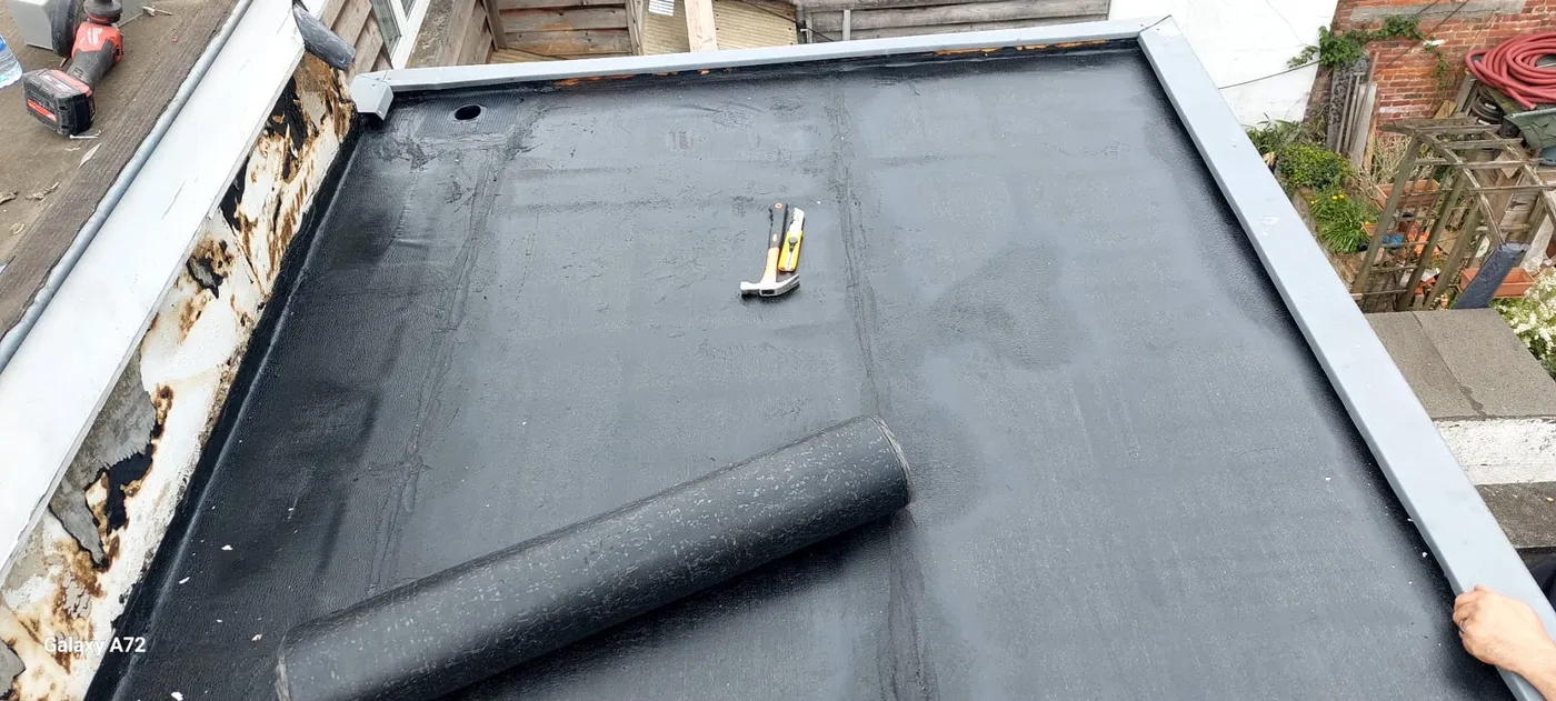Pose d'étanchéité sur une toiture plate, rouleau et outils visibles.