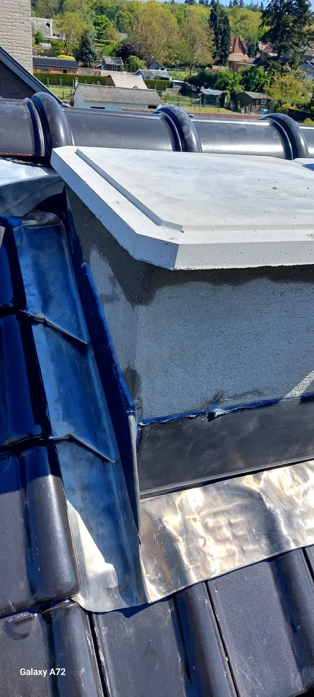 Souche de cheminée et zinguerie en cours sur une toiture en tuiles.